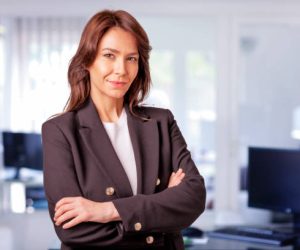 Attractive mid aged businesswoman wearing blazer and standing at the office. Confident professional woman looking at camera and smiling.